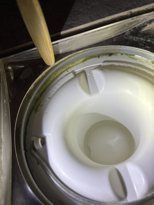 Klämring med fogmassa runt kanten och ett verktyg som petar, visar grönt material under klämringen i närbild.