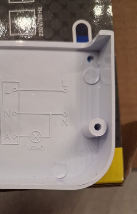 Plastlåda med el-schema för anslutning av ledare markerade L, N och A samt en lastsymbol, del av en kopplingsdosa eller elektrisk komponent.