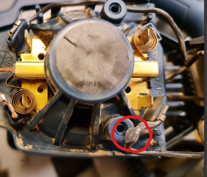 Närbild av ett kretskort med motoranslutning, en klämd kabel visas i rött, omgiven av plast- och metallkomponenter från en elektrisk enhet.