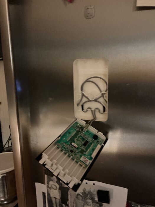Öppnat panel på kylskåpsdörr visar exponerat kretskort och kablar.