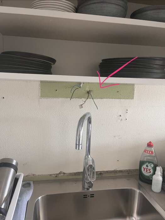 Elkablar sticker ut från väggen ovanför diskbänken, markerade med en rosa pil. Överskåp och tallrikar syns ovanför.