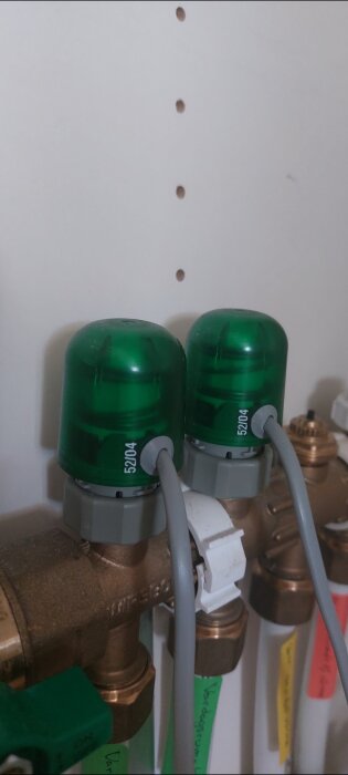 Två gröna styrdon med kablar anslutna till en kopparrörinstallation, märkta med "52104".
