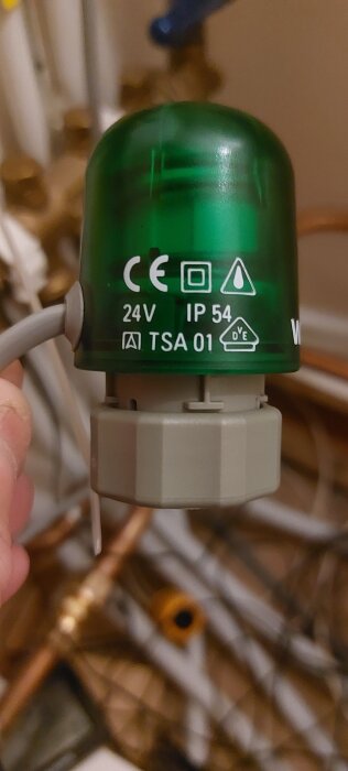 Närbild av ett Wirsbo styrdon med märkning 24V, IP54 och TSA 01, grönt hölje och grå bas, i ett rörligt installationsområde.