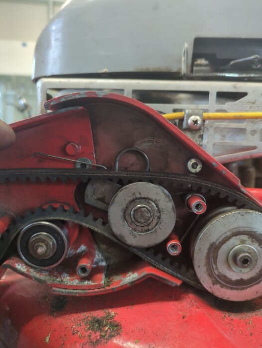 Röda maskindelar med kugghjul och rem i närbild, del av ett motor- eller maskinsystem.