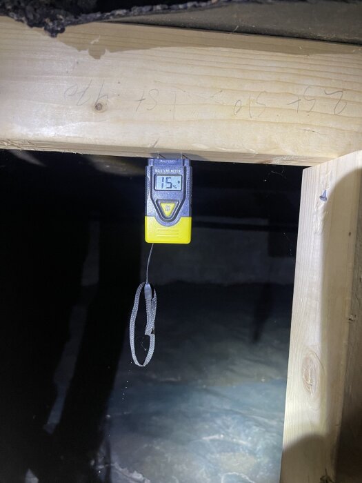 Fuktmätare visar 15% i träbjälke i krypgrund med plastgolv, tydlig upphängning och trästruktur synlig.