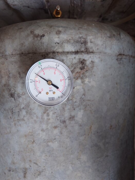 Tryckmätare på en hydrofor visar ett tryck mellan 0 och 8 bar. Hydroforens yta är rostig och sliten.