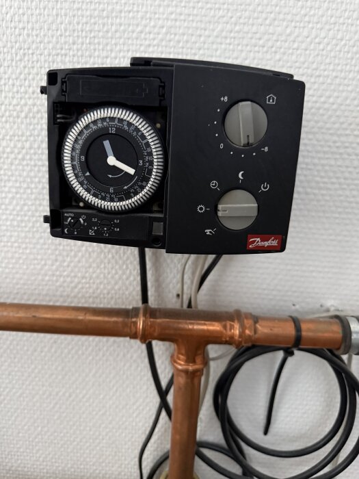 Timer med reglage på en värmeanläggning, kopplad till en kopparledning. Enhet med rattar för att justera temperatur från -8 till +8 grader.