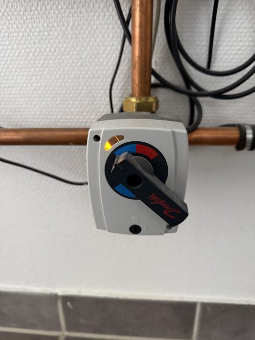 Elektriskt reglage på rör med Danfoss-logga och färgkodning i rött och blått. Belysning indikerar justering.