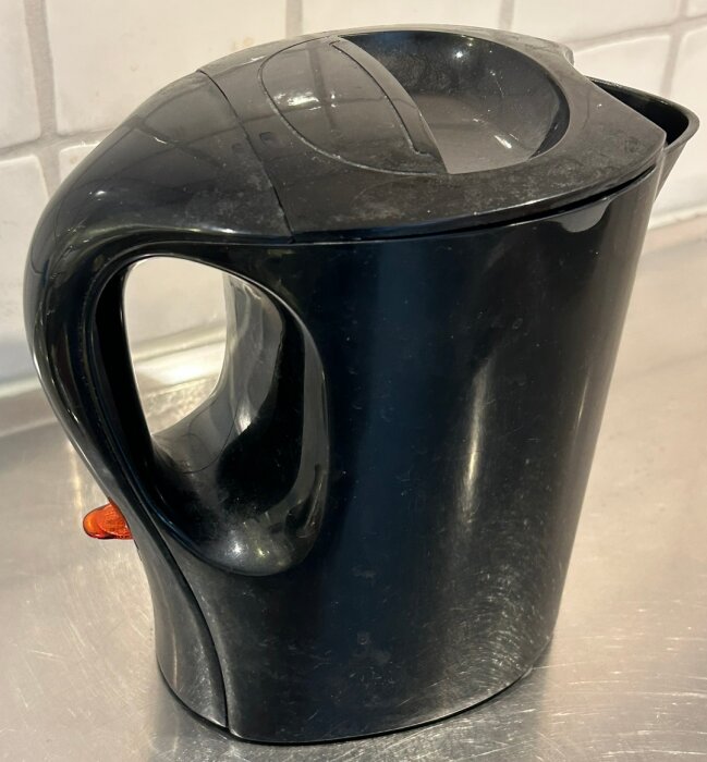 En svart vattenkokare på en köksbänk med en orange indikatorlampa.