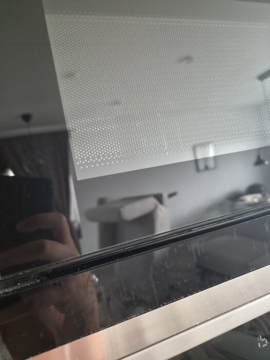 Mikrovågsugnens panel med missfärgningar efter rengöring, liten spegling av rummet syns i glaset.