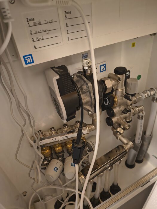 Rörligt system med ställdon och rörkopplingar, märkta zoner och elkablar i ett skåp, del av ett byggprojekt för värmesystem.