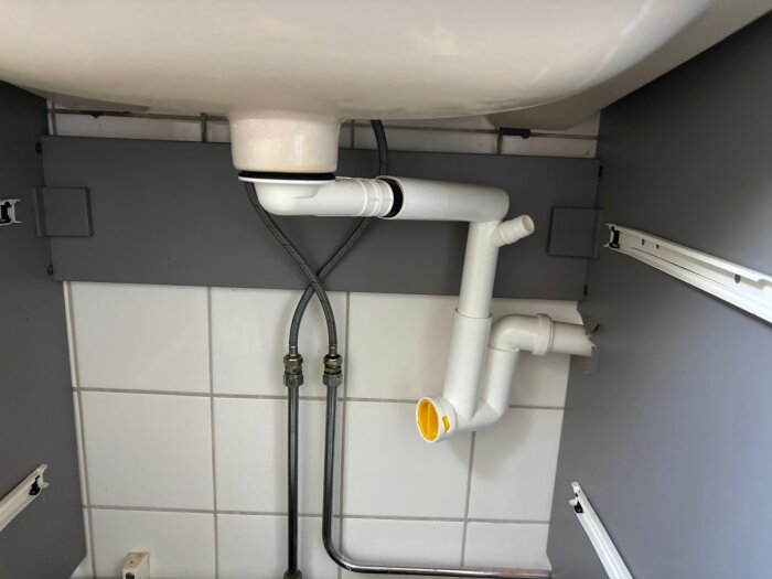 Avloppsrör under ett handfat med en guldragering som en person försöker lossa för att rensa avloppet; rör och kopplingar synliga.
