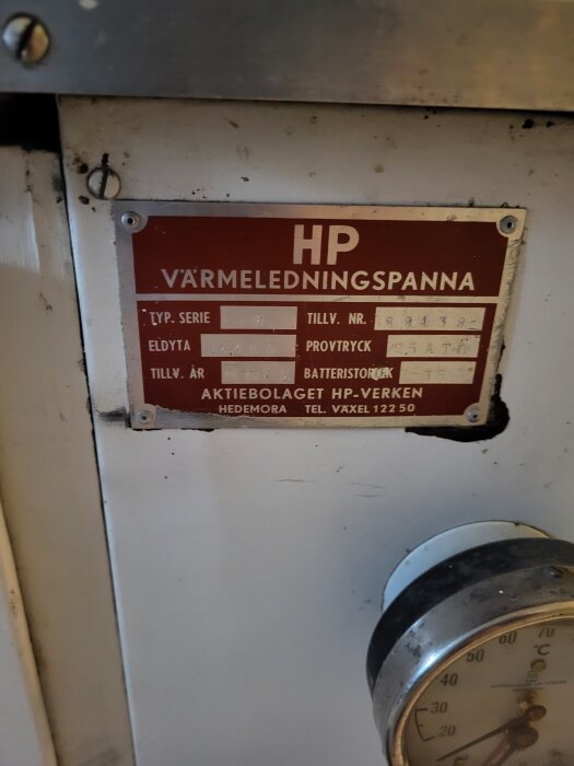 Närbild av en äldre HP värmeledningspanna med modellskylt och en temperaturmätare.