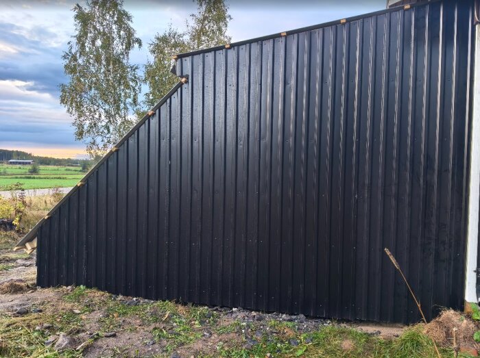Svartplåttak på ett bygge, nyss monterat med sned sektion till vänster och skog i bakgrunden. Testar olika metoder för att få korrekt passform.