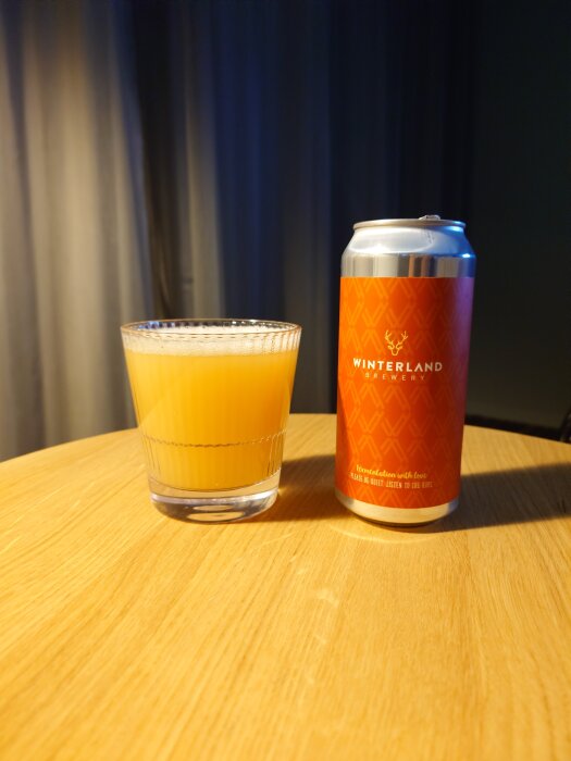 Ett glas med gul dryck bredvid en röd burk märkt "Winterland Brewery" på ett bord.