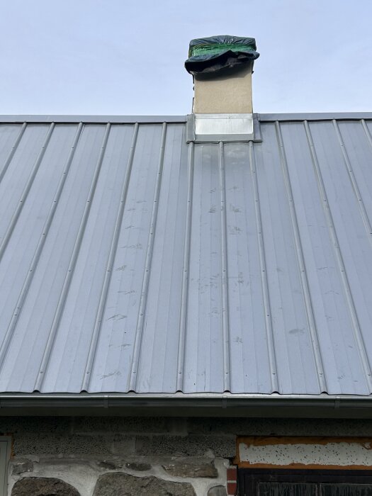 Plåttak med skorsten, fläckar synliga på ytan; skorstenen är delvis täckt med plast.
