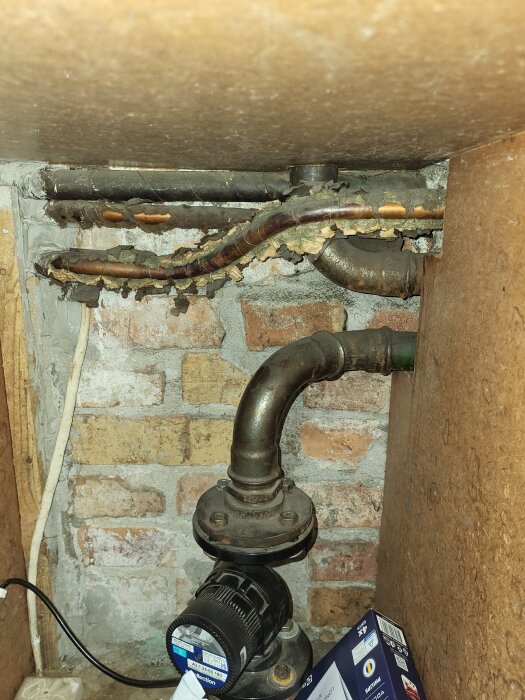 Rörsystem i tegelvägg med plastkopplingar och metallrör, kablar synliga, förmodligen relaterat till ett byggprojekt eller renovering.