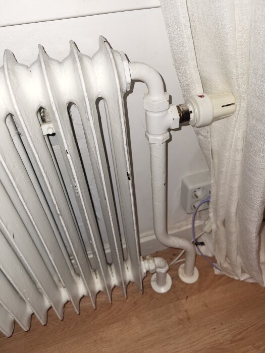 Element med rörsystem mot en vit vägg och intilliggande gardin.