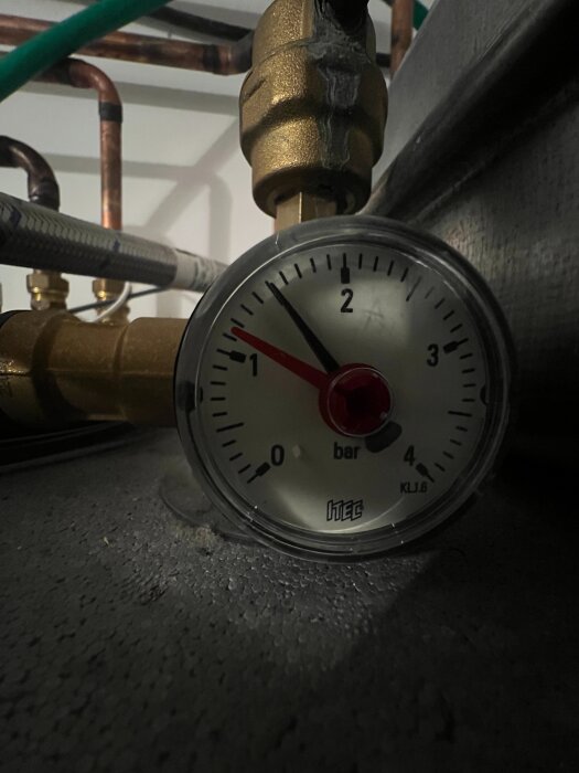 Manometer visar tryck på cirka 1,5 bar i ett rörsystem, med synliga kopparrör och ventiler i bakgrunden.