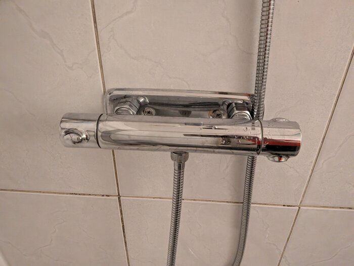 Kromfärgad duschblandare från Hansgrohe monterad på kakelvägg, med kopplade slangar och synliga droppar på ytan.