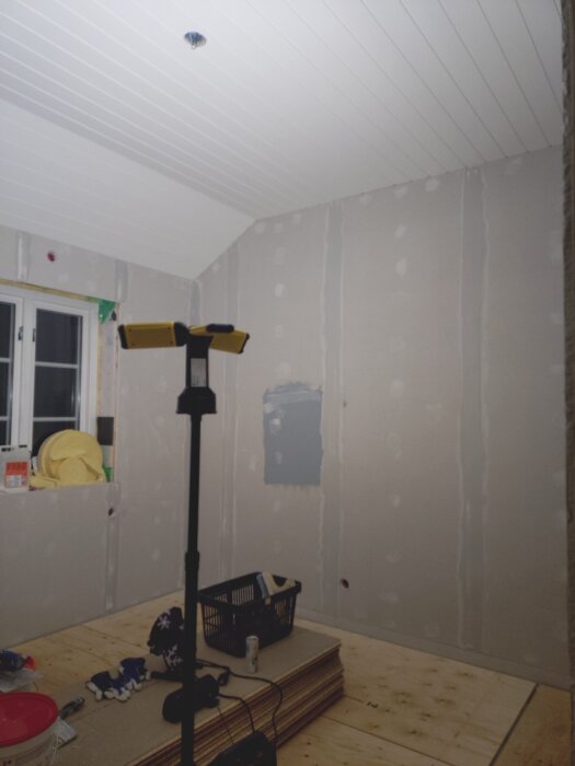 Rum under renovering med arbetslampa som lyser upp väggar och golv.