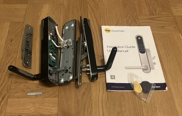 Begagnat Yale Doorman låsset med installationsmanual, monteringsplatta, och tillbehör på ett trägolv.