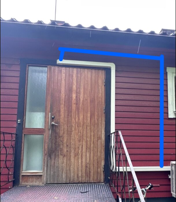 Röd trävägg med brun dörr och ett kanalrör som löper runt dörren, illustrerat med en blå linje, som leder till en luftvärmepump.