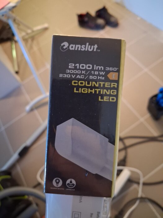 LED-armaturförpackning från Anslut med specifikationer, inklusive 2100 lumen, 3000K, 18W och 230V, fotograferad på kaklat golv.