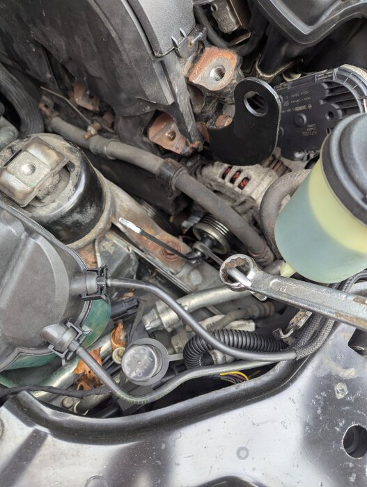 Motorutrymme med synlig generator, verktyg och bortkopplade motorfästen under reparation av generatorns frihjul.