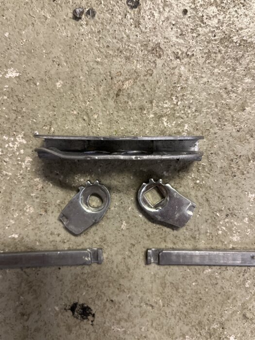 Metallkomponenter på grov betongyta, inkluderande två ankarplattor, två låsbrickor och två metallstänger.