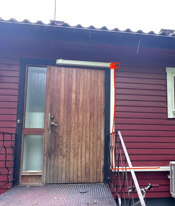 Röd trävilla med ytterdörr, trappa och ett rött streck på fasaden som markerar en planerad kanaldragning inomhus.