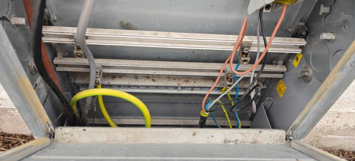 Elskåp med exponerade kablar, visar flera ledningar med färgkoder. Markskåp öppet för installation av solceller. Bristande anslutning synlig.