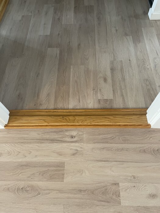 Ljus parkettgolv med en trätröskel i kontrasterande orange ton.