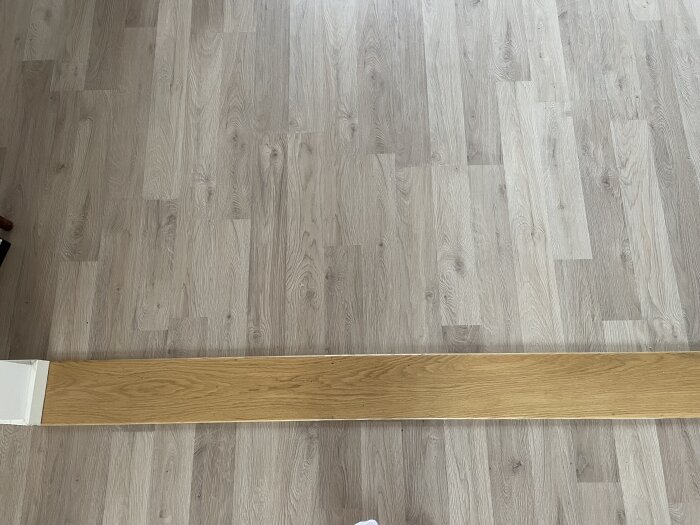 Ljust golv med en mörkare tröskelplanka ovanpå, som inte matchar golvets färgton.