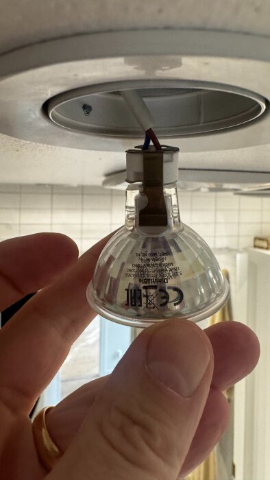 En hand håller i en LED-lampa monterad i en infälld spot.