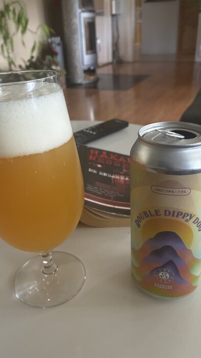 Ett glas med skummig öl bredvid en ölburk märkt "Double Dippy DOU IPA" och en bok av Håkan Nesser på ett bord.