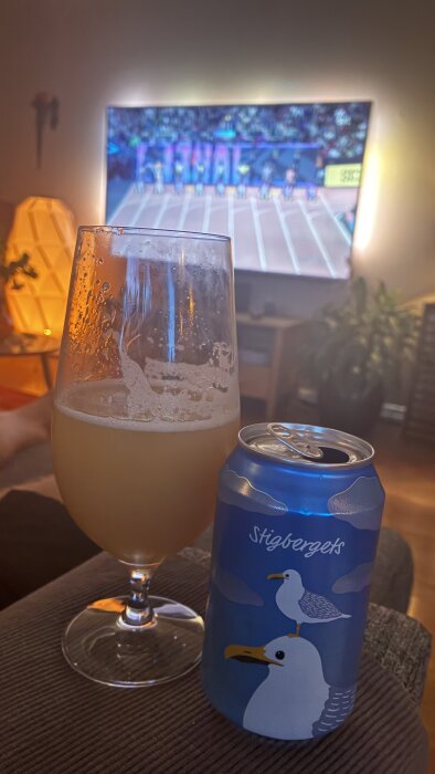 Ölglas och burk med måsmotiv från Stigbergets, bakgrund visar ett friidrottsevenemang på TV.