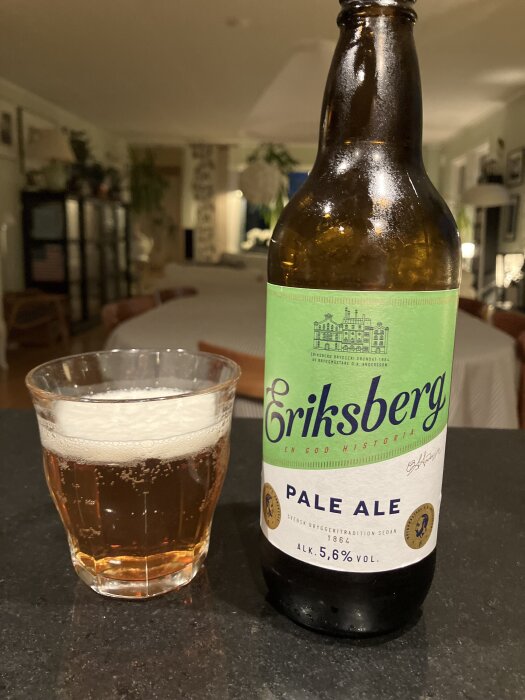 Flaska Eriksberg Pale Ale med glas bredvid, placerad på ett bord i ett vardagsrum.