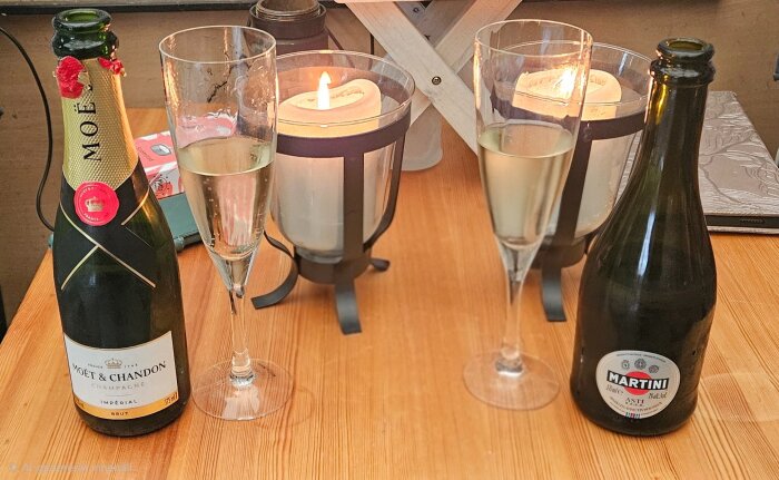 Champagneflaska av Moët & Chandon och Martini Asti-flaska på ett bord med två tända ljus och champagneglas.