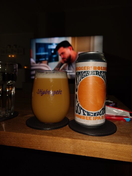 Stigbergets-ölburk och glas med öl på bord, TV i bakgrunden.
