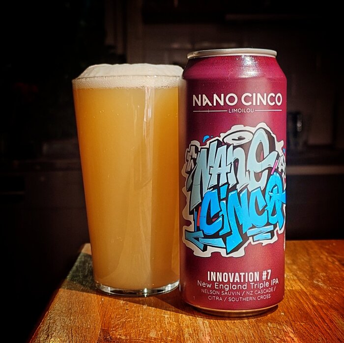 En burk med Nano Cinco New England Triple IPA och ett fullt glas öl på ett bord.