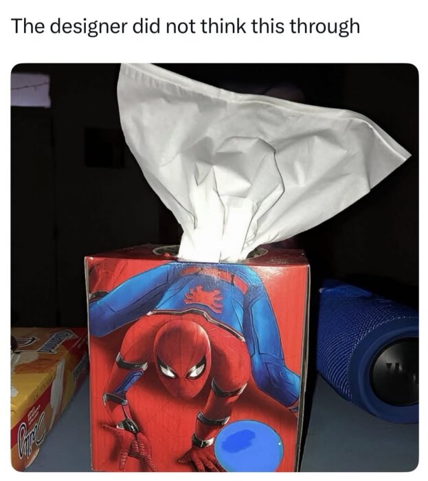 Tissue box with Spider-Man design, tissues poking out of his rear, humorous oversight in packaging.