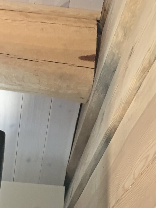Timmerstomme i nybyggt hus där en stock har vridit sig, visar sprickor och möjliga monteringsbrister, med närbild av stockens ända och intilliggande plankor.