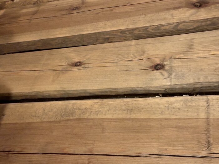 Närbild av timmer i ett nybyggt hus där vissa stockar är skeva och det finns synliga mellanrum.