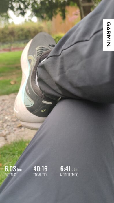 En person i träningsbyxor och löparskor vilar på en parkbänk, Garmin-data visar distans 6,03 km, total tid 40:16, medeltempo 6:41/km.