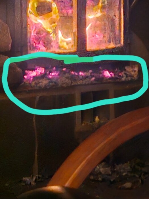 Brinnande eldstad med glödande kol och tegeldetaljer, omgiven av en blå markering i förgrunden.