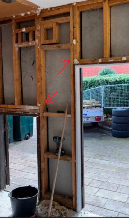 Trästomme med reglar ovanför fönsteröppning, röda pilar markerar stående reglar från golv till tak; synliga verktyg och material i bild.