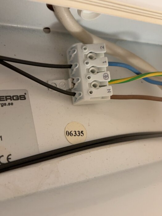 Elektrisk kopplingsplint med fem anslutningar och kablar i olika färger syns, monterad på en vit yta.