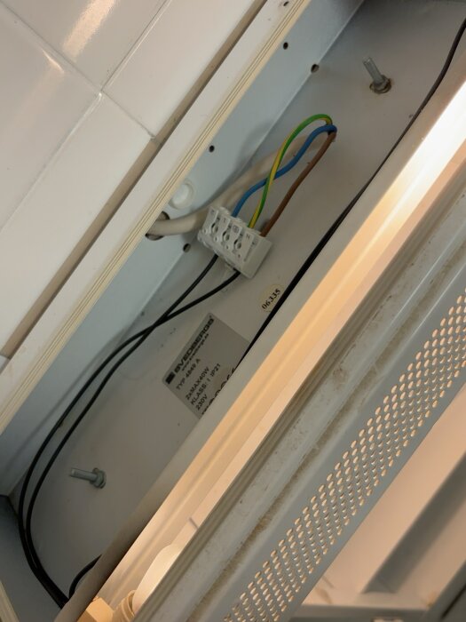 Elektriska kablar och kopplingsplint inuti ett badrumsskåp där en lampa har tagits bort för att bytas ut.