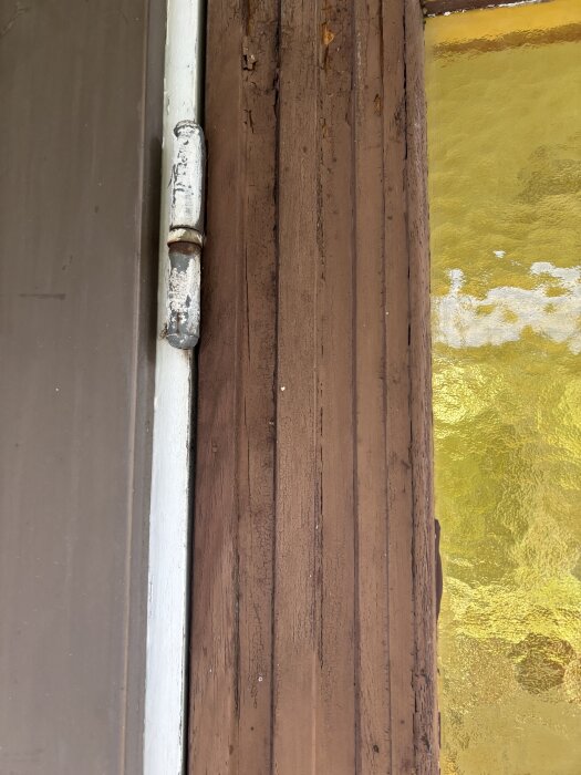 Dörrkarm med slitet gångjärn bredvid guldfärgat glas.